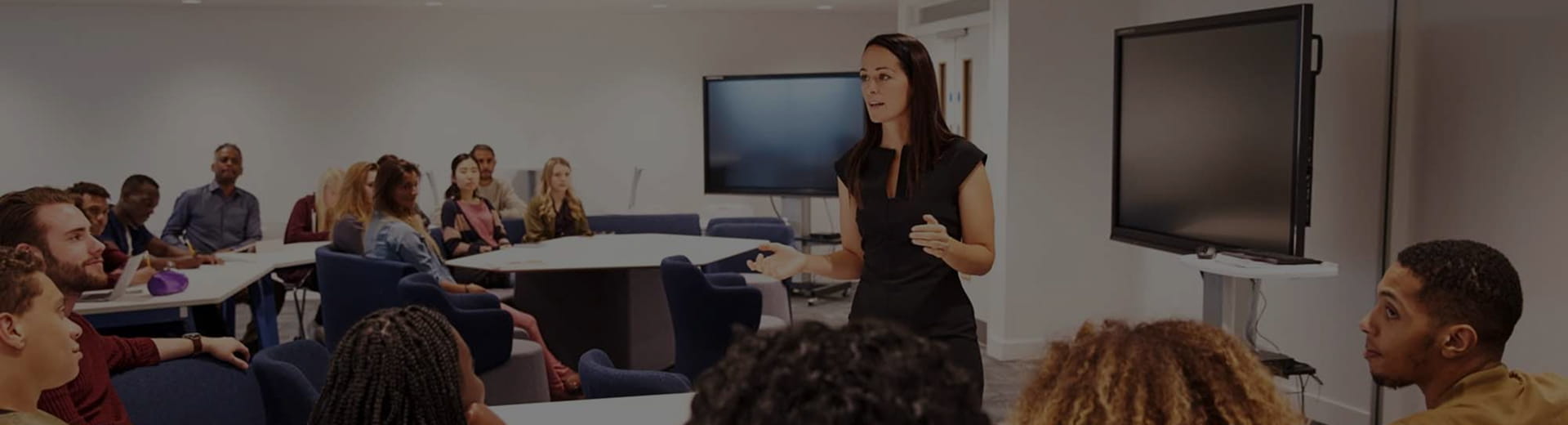 educator presenting to students in a modern classroom with display screens 